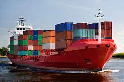 A red-colored, fully loaded cargo ship over the sea