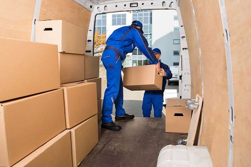 Blue uniformed worker inside a delivery van, giving a parcel to the distributing agent